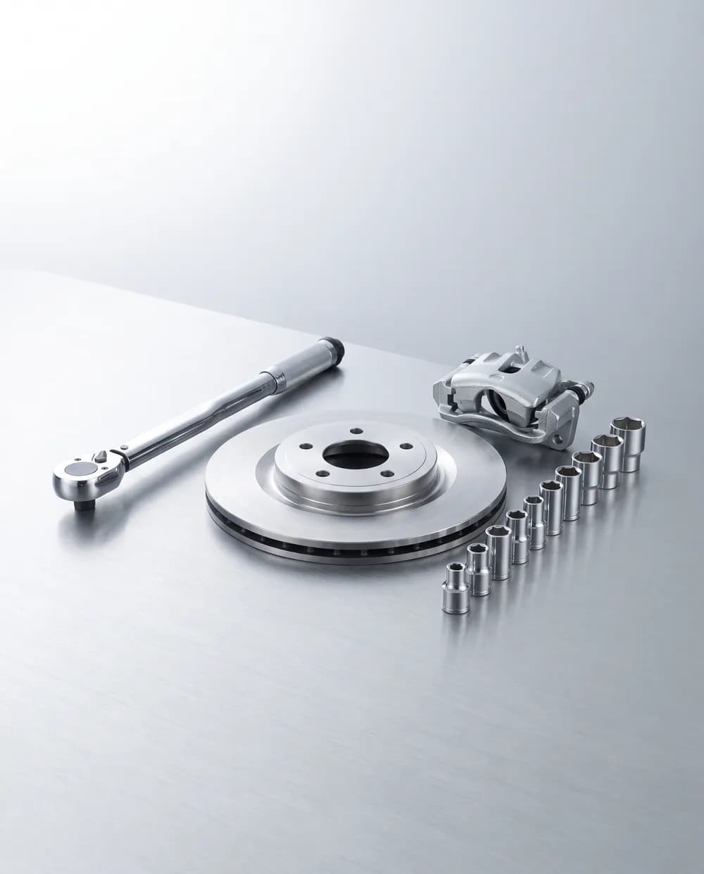 Drehmomentschlüssel, neue Bremsscheibe, Bremssattel und Steckschlüsseleinsätze auf einer Werkbank — Symbolbild